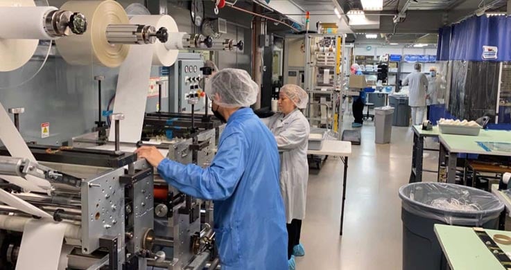 Cleanroom-Contract-Manufacturing-737x390-1 clean room precision converting on a multi station rotary die cutting machine with several technicians in clean room apparel at Boyd